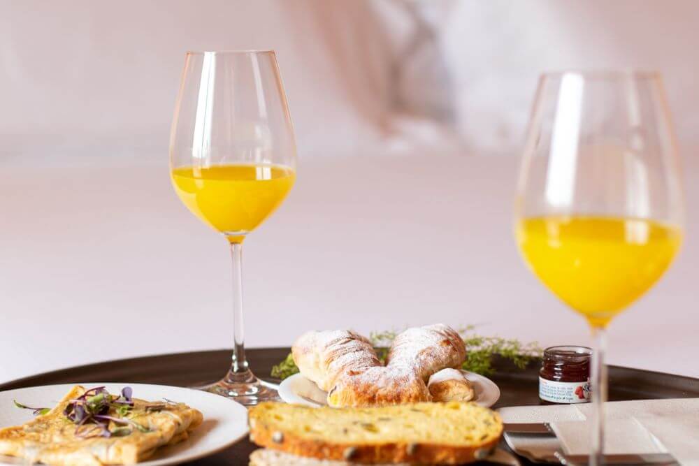 A table with two glasses of wine filled with juice and bread and pastries.