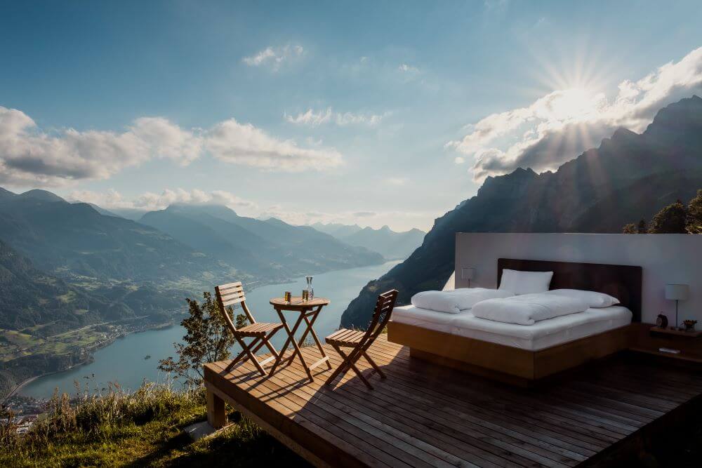 A bed outside overlooking a lake in the middle of moutains